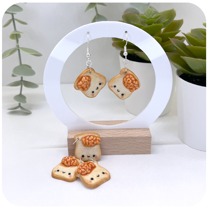 Kawaii baked beans on toast earrings handmade from polymer clay, featuring cute orange beans on golden toast slices.