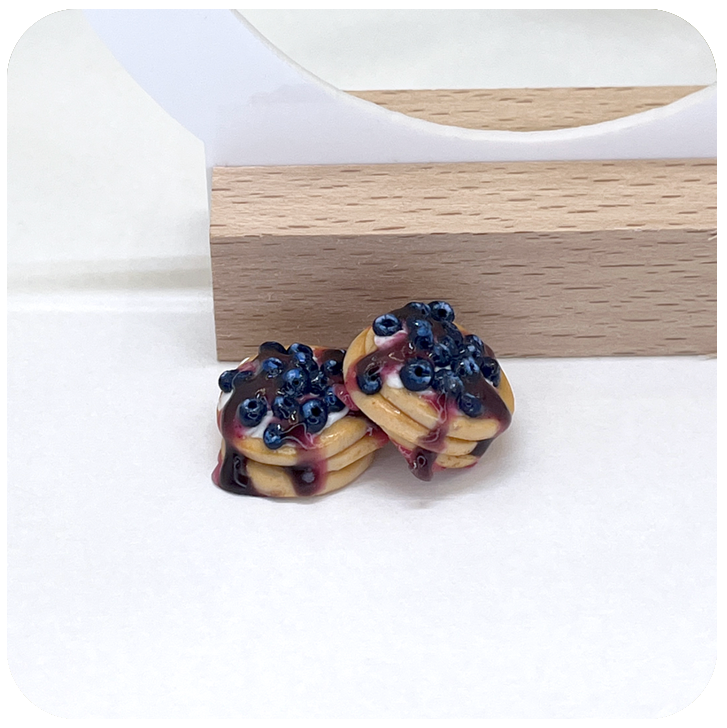 Close-up of realistic pancake earrings with blueberries and cream, handmade from polymer clay with lifelike detail and shine.